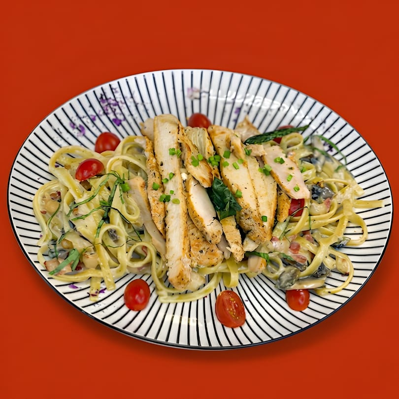 Creamy fettuccine pasta with sliced chicken, cherry tomatoes, and herbs on a striped plate.