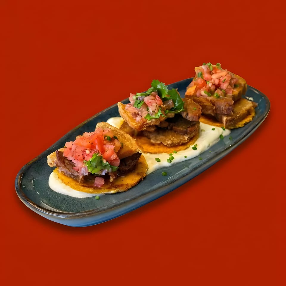 Three mini tacos with meat, salsa, and cilantro on a dark blue plate with white sauce.