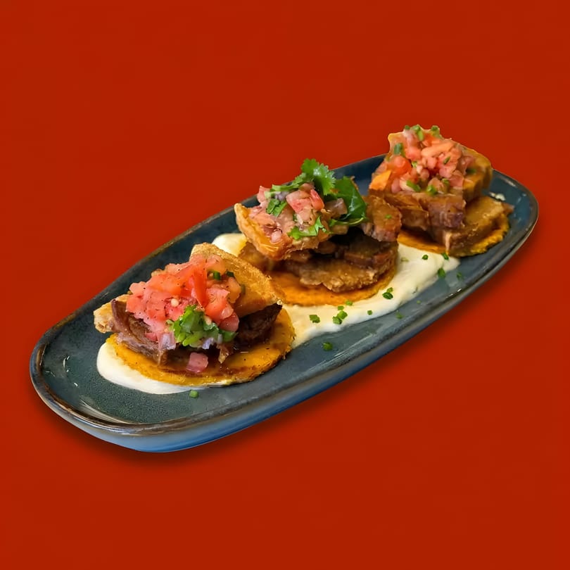 Three mini tacos with meat, salsa, and cilantro on a dark blue plate with white sauce.