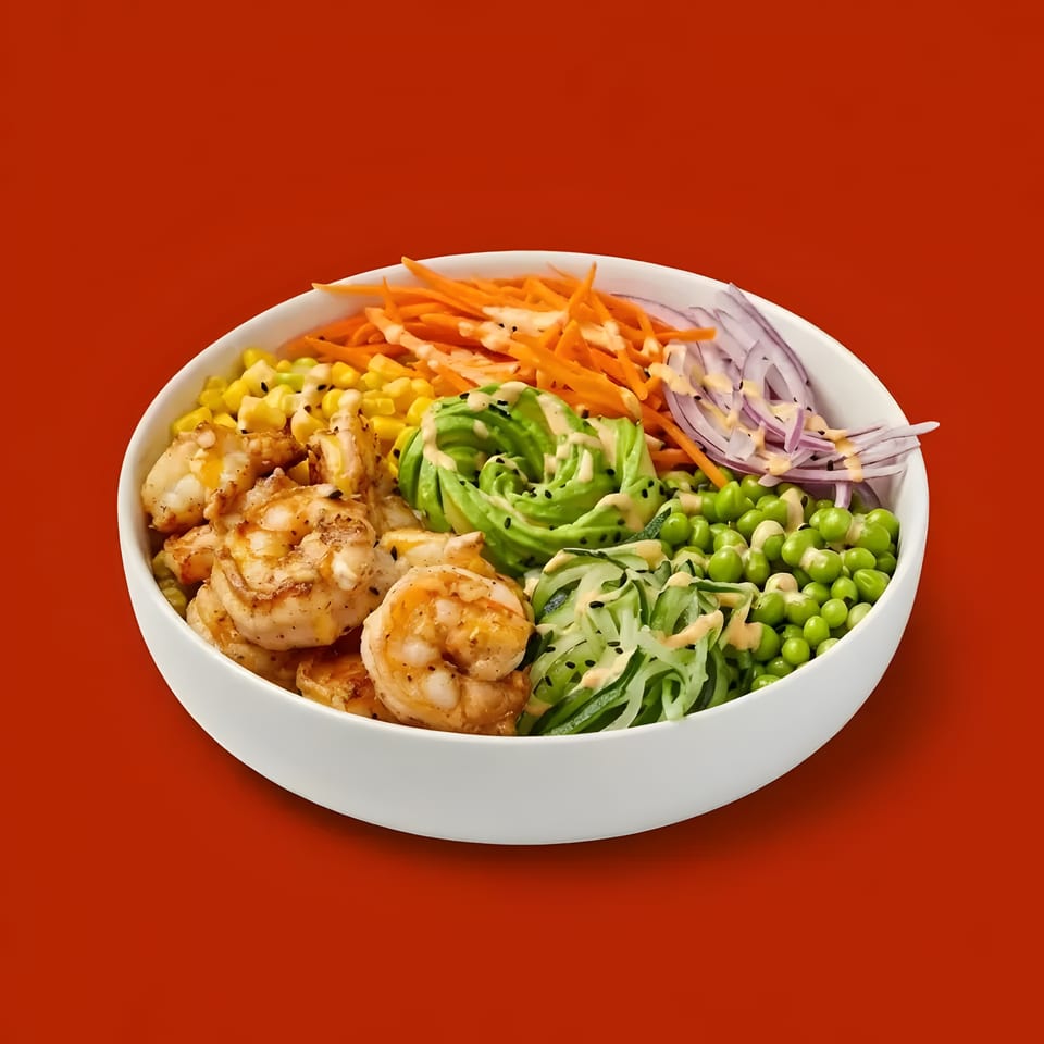 A white bowl filled with shrimp, corn, avocado, carrots, red onion, peas, and cucumber noodles.