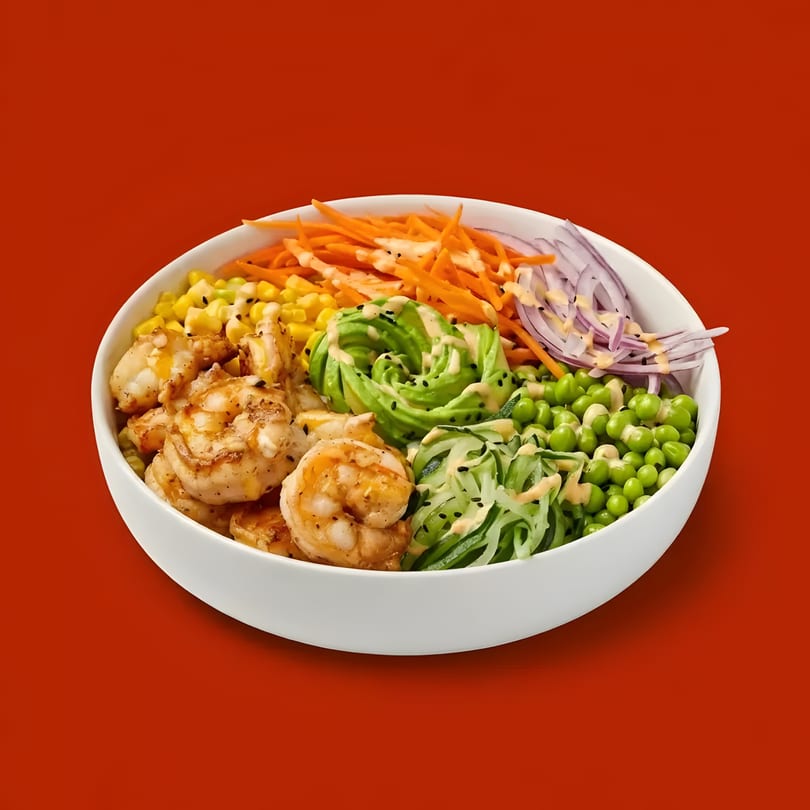 A white bowl filled with shrimp, corn, avocado, carrots, red onion, peas, and cucumber noodles.