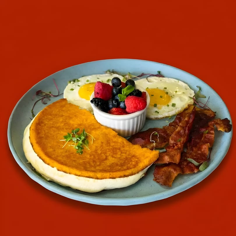 Breakfast plate with a large omelet, two fried eggs, crispy bacon, and a side of fresh berries.